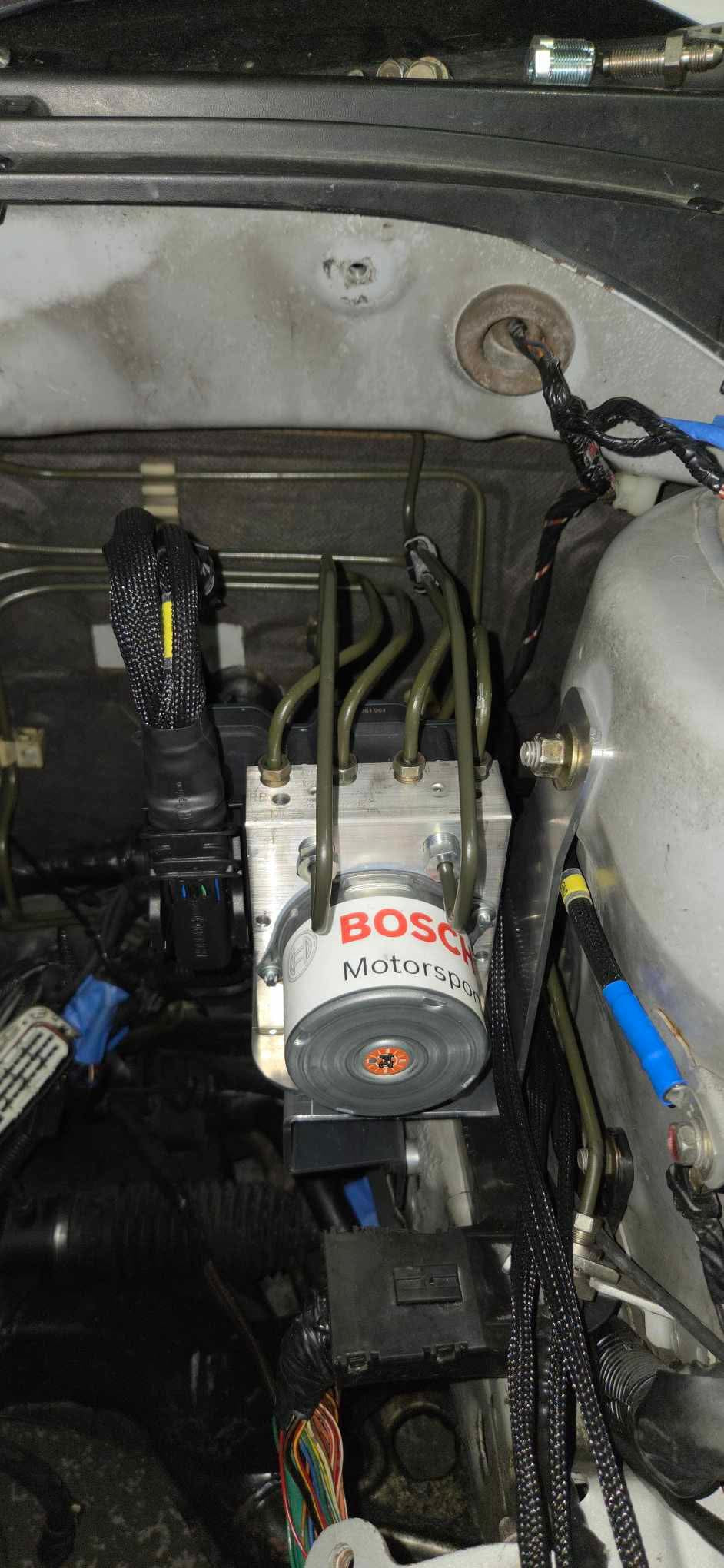 Bosch Motorsport ABS M5 hydraulic unit on its 909 bracket in a Mitsubishi EVO 7-9 engine bay with formed brake hard lines